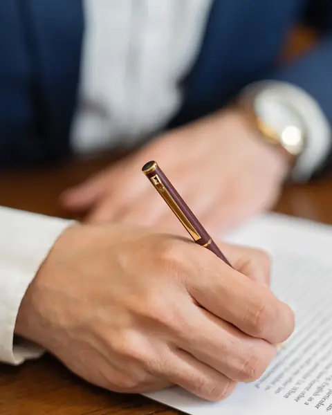 Symbolbild: Hand mit Füller über einem Dokument am Schreibtisch einer Kanzlei